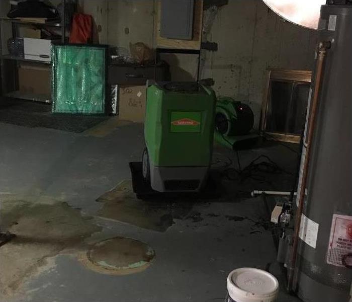 Green dehumidifier on a basement floor near a water heater. 