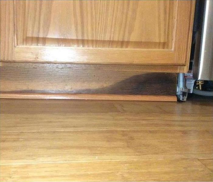 Brown kitchen cabinet with water damage on the bottom.