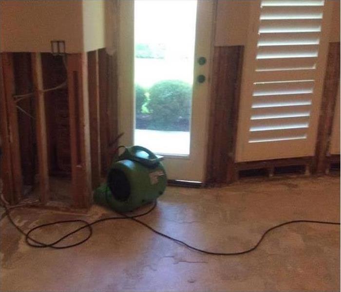 Wood floor removed with a green SERVPRO air mover in the background.