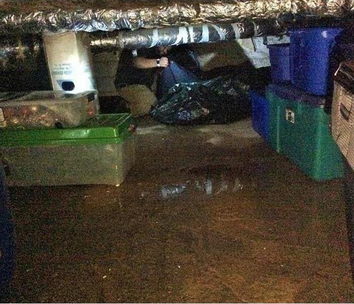 Wet crawl space with standing water on the floor and blue and green tubs in the background.
